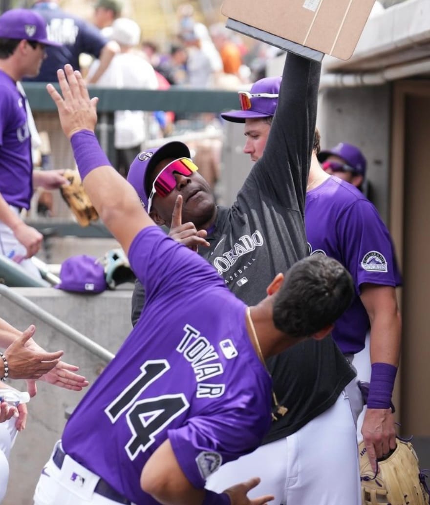 Tovar and Meulens celebrate in the dugout after something awesome has happened. Tovar wears a purple jersey while Meulens rocks some mirror sunglasses and holds a clipboard.