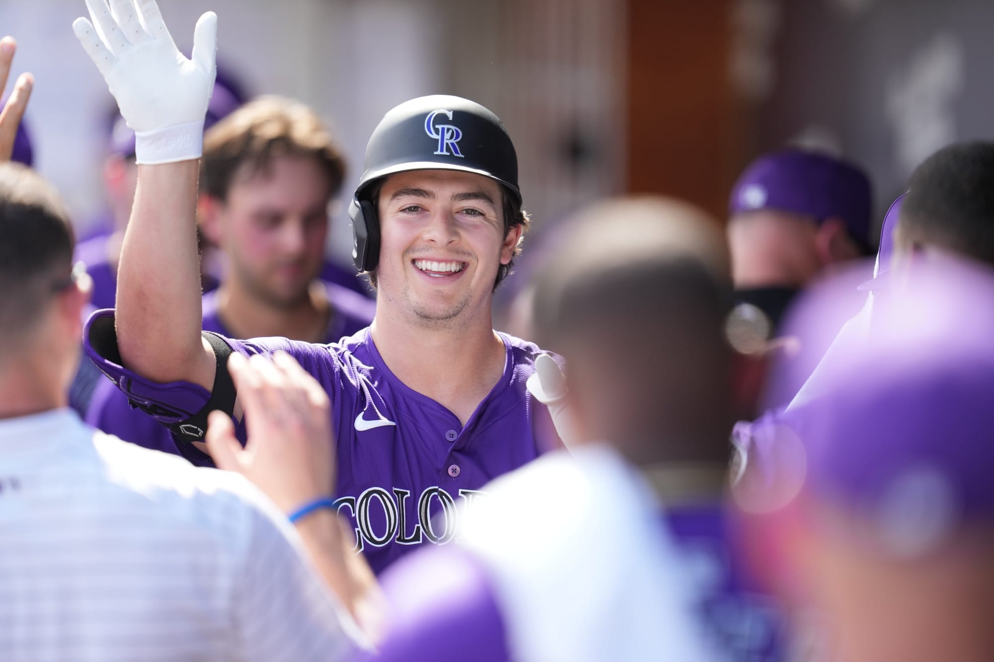 Michael Toglia celebrates in the dugout. He’s wearing a purple jersey, smiling, and high-fiving his teammates.