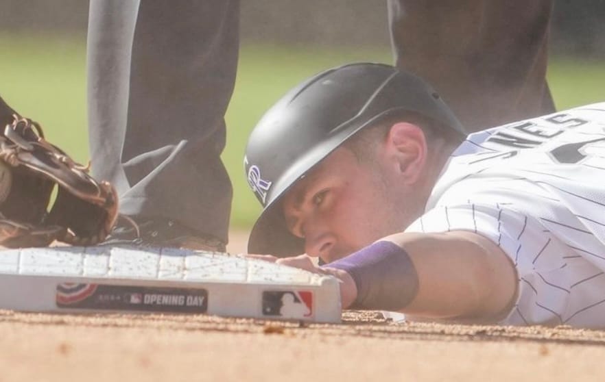 Nolan Jones reaches out to touch second after stealing a base. The photo is focused on his face. He’s wearing a batting helmet and purple pinstripes.