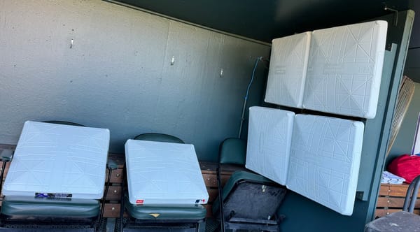 Six white bases are stored in the Rockies’ Coors Field Dugout. Two rest on green chairs.